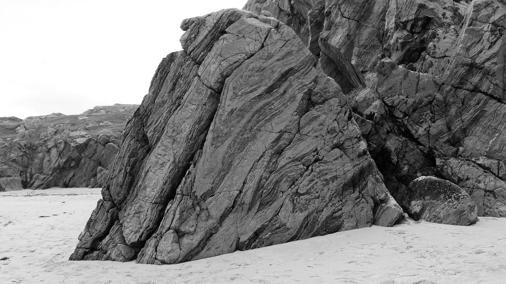 a large slab of rock juts out of a beach